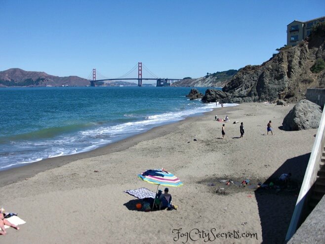 China Beach, sunbathers on beach and Golden Gate Bridge view.